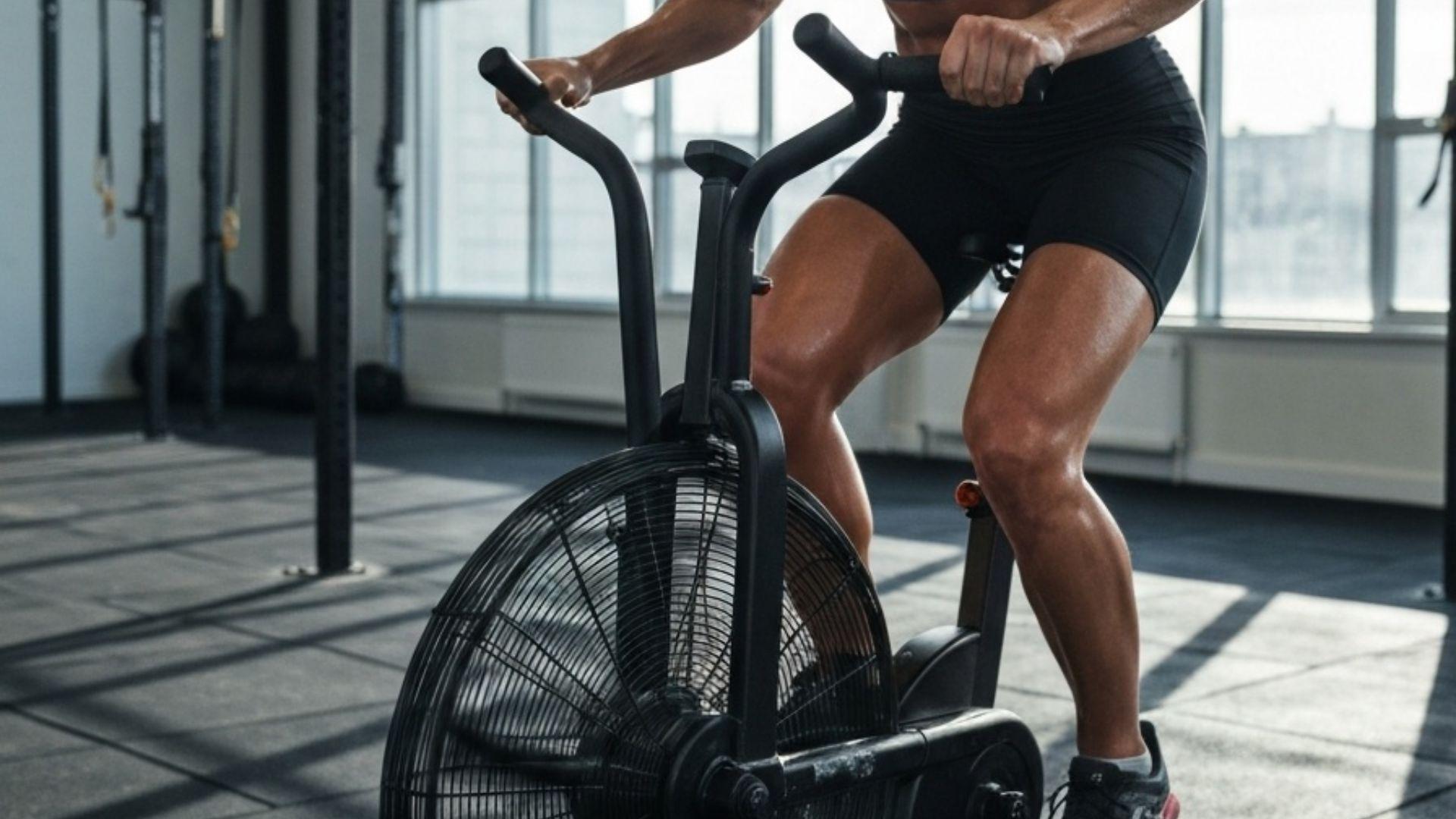 Treningsutøver som svetter og tråkker hardt på en svart airbike i et moderne CrossFit-treningssenter