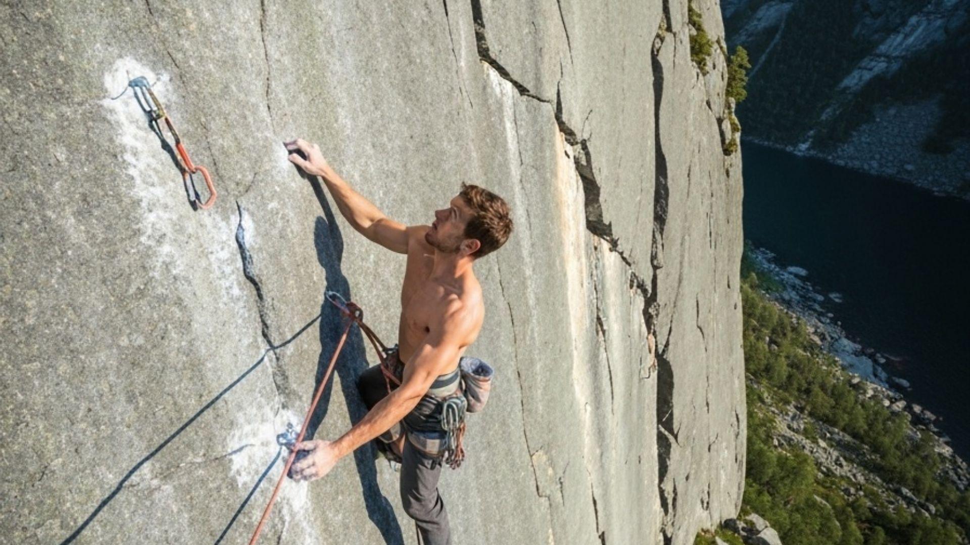 Klatrer leder sportsklatre-rute pa norsk fjellvegg med tau klippet i bolter
