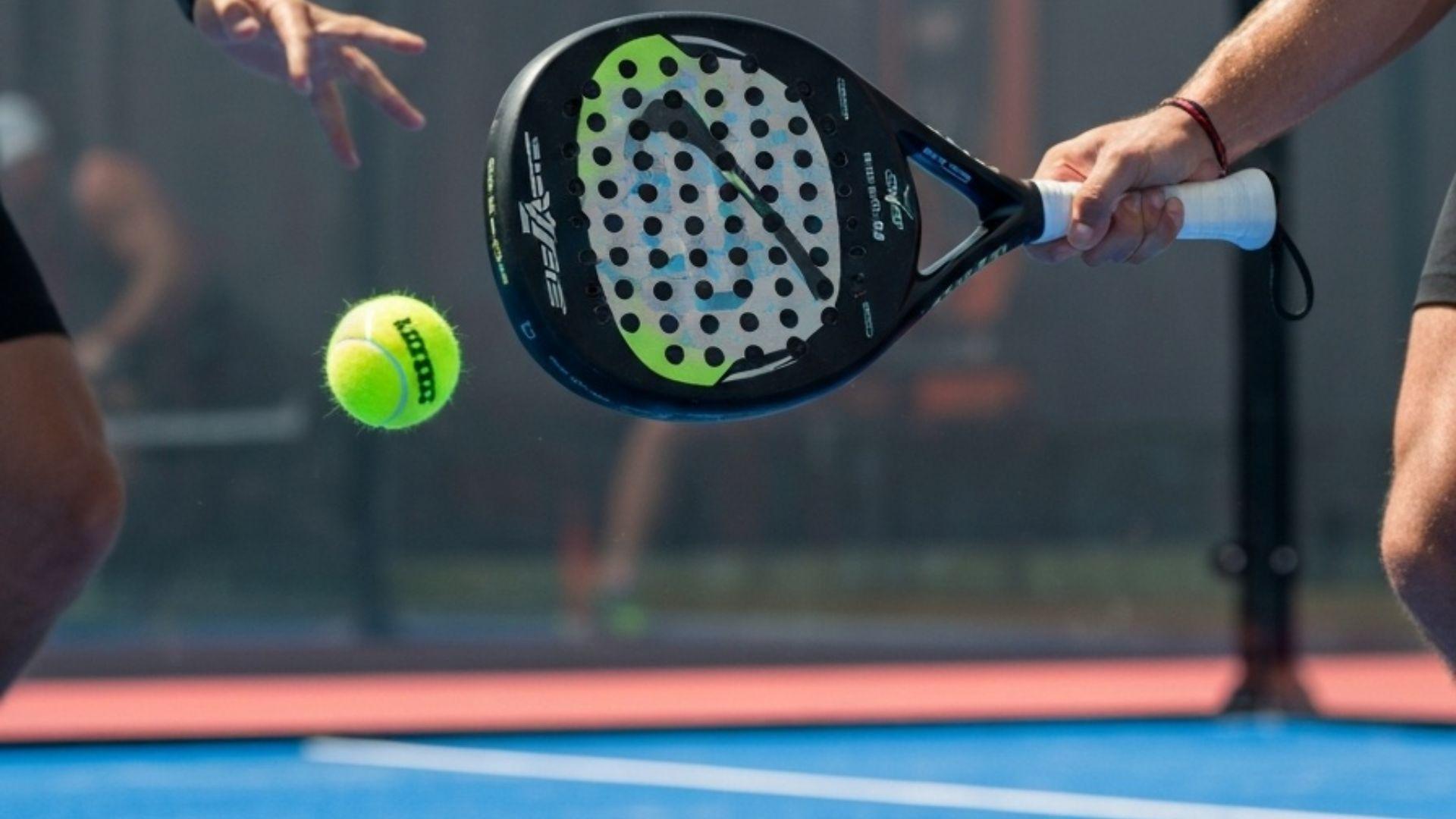 Padelracket som treffer ball på padelbane i dagslys