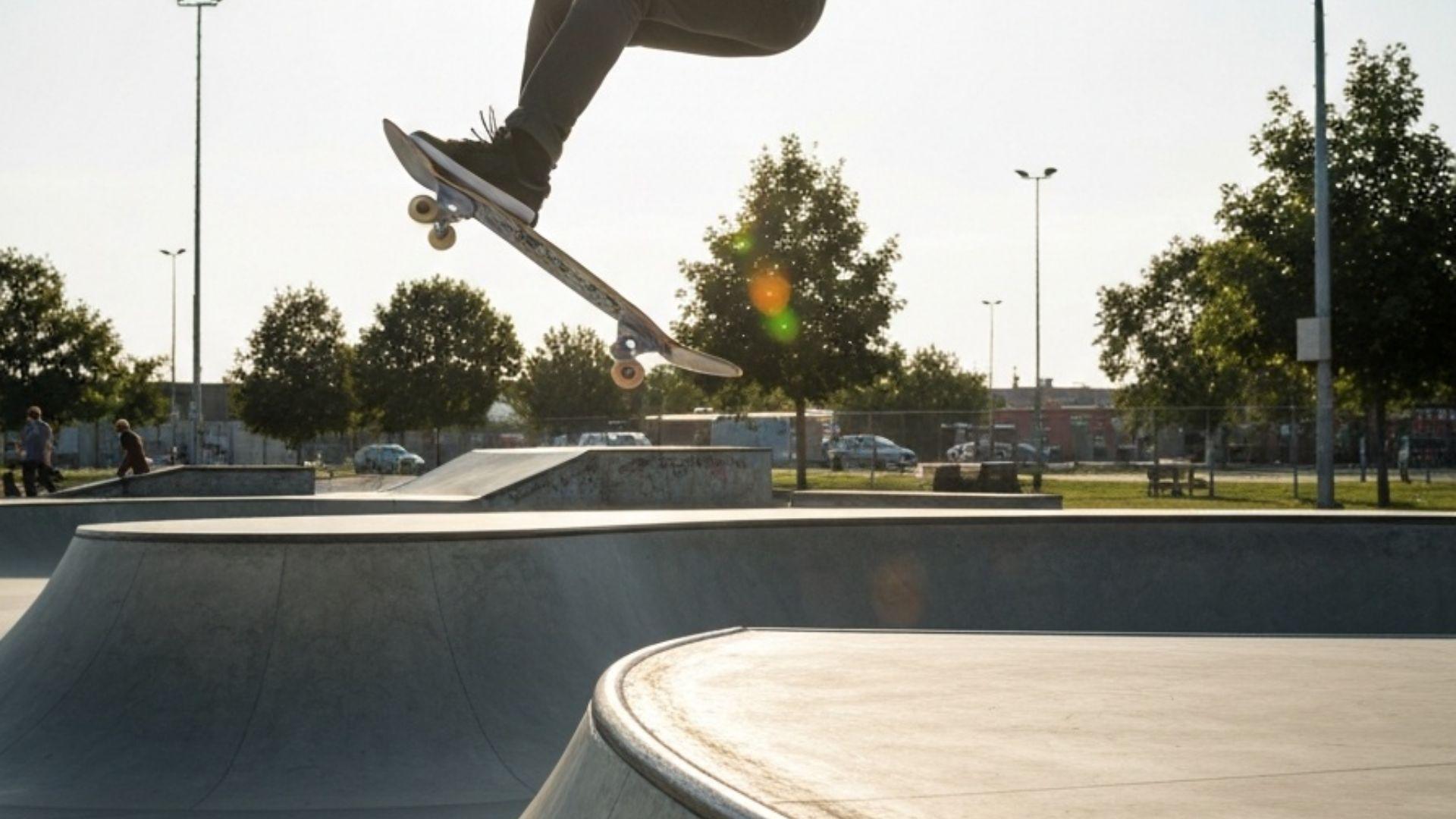 Skateboarder som gjør kickflip i betong-skatepark i ettermiddagssol