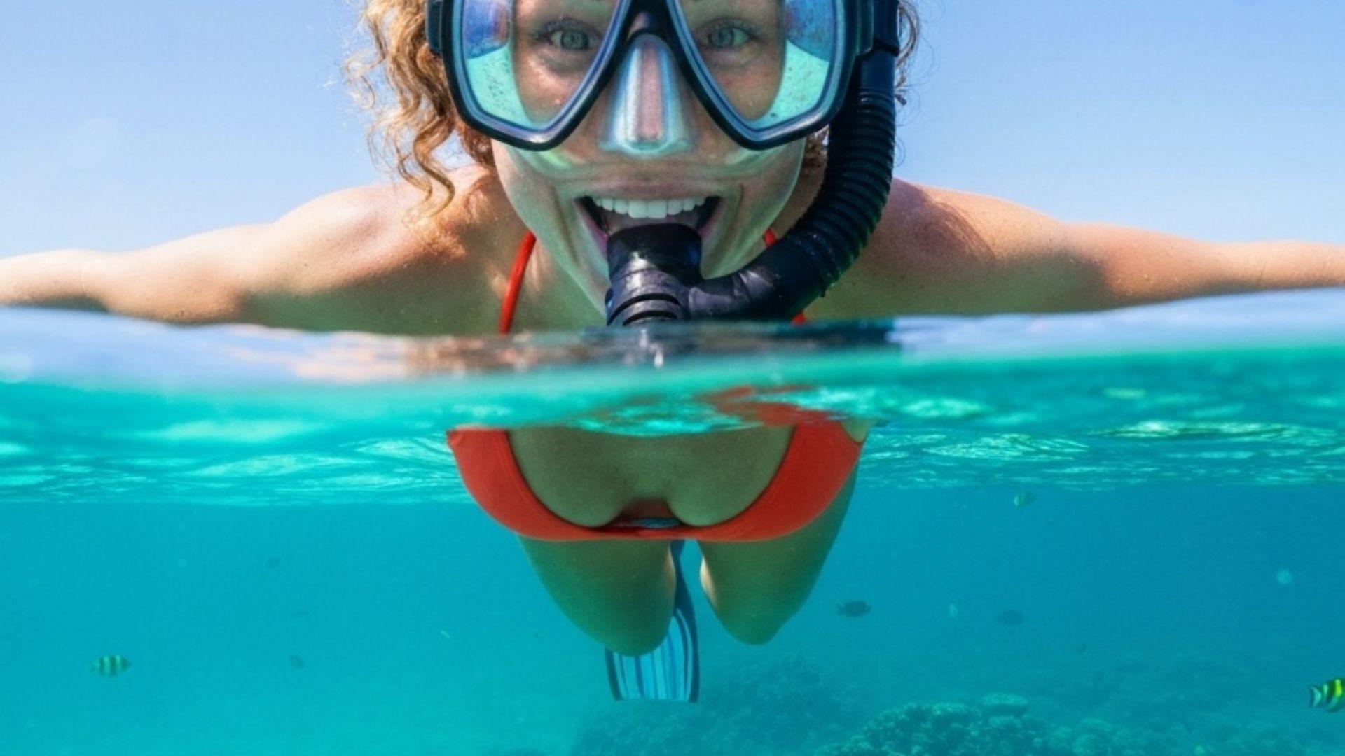 Kvinne som snorkler i krystallklart turkist vann med korallrev
