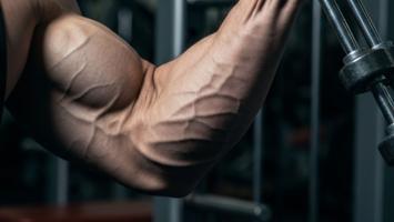 Sterk hånd som griper en metallgrippetrener med muskuløs underarm