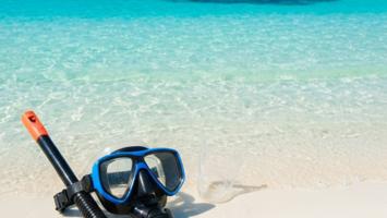 Dykkermaske og snorkel på sandstrand med krystallklart hav