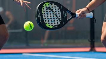 Padelracket som treffer ball på padelbane i dagslys