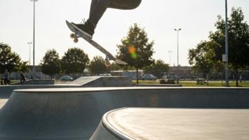 Skateboarder som gjør kickflip i betong-skatepark i ettermiddagssol