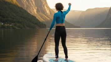 Kvinne padler stand-up paddleboard pa en stille norsk fjord i soloppgang