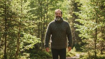 Person i tykk ullgenser gar i norsk skog i varmt naturlig lys